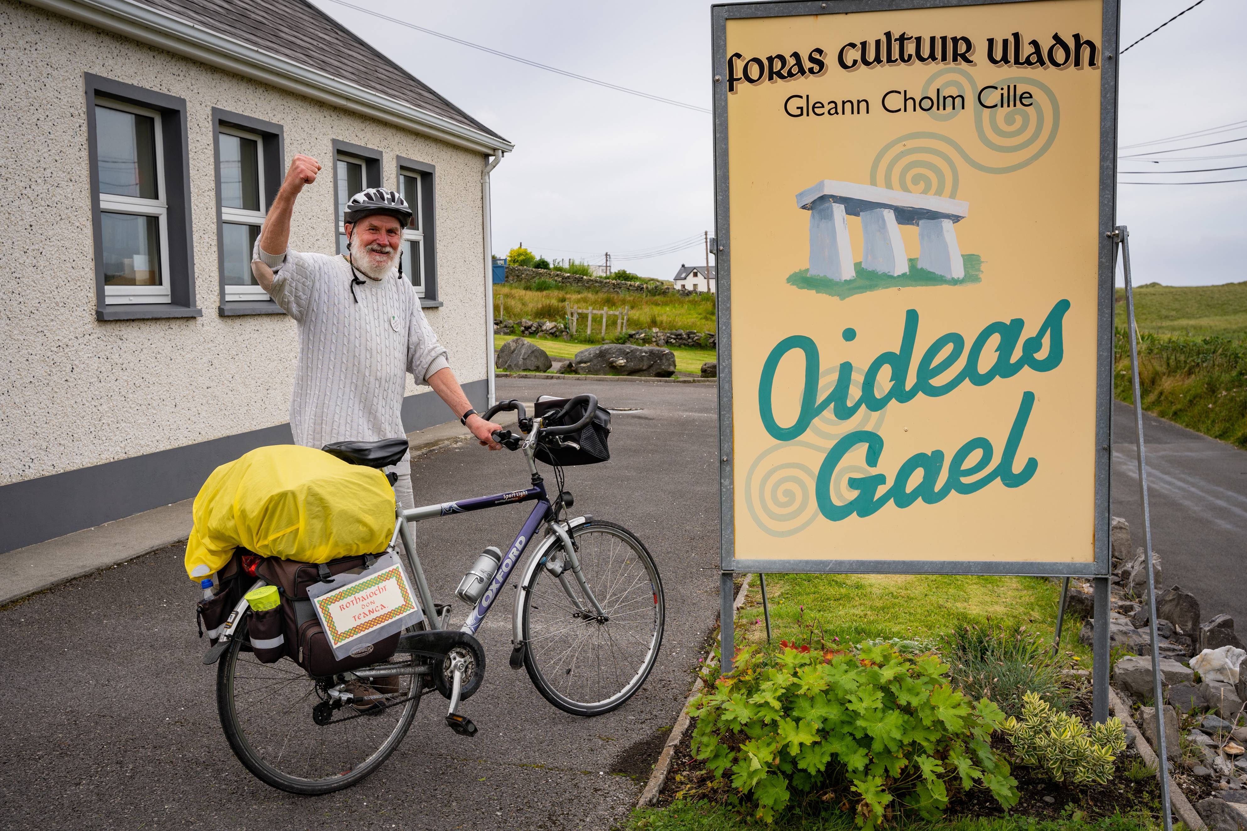 Frans D'Hooge ar a rothar in aice le comhartha bóthair Oideas Gael