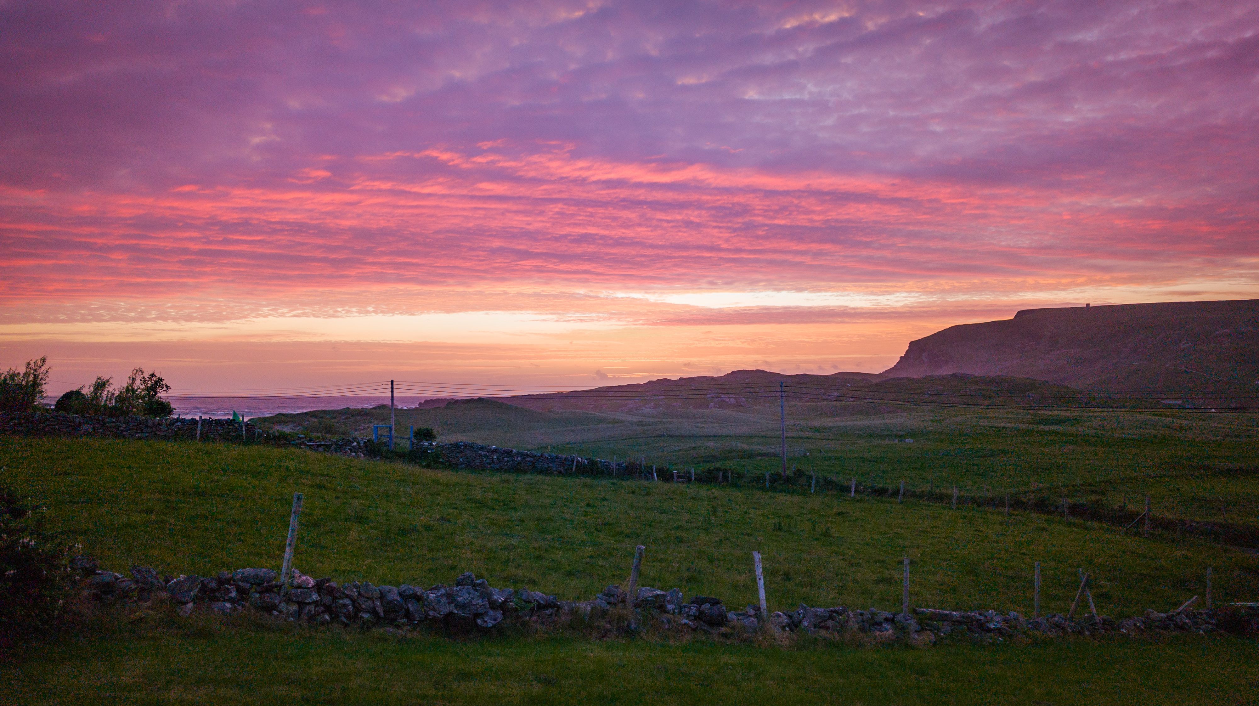 Luí na gréine os cionn na Dumcha, Gleann Cholm Cille, agus dathanna idir bhuí, bhándearg agus dúghorm sa spéir