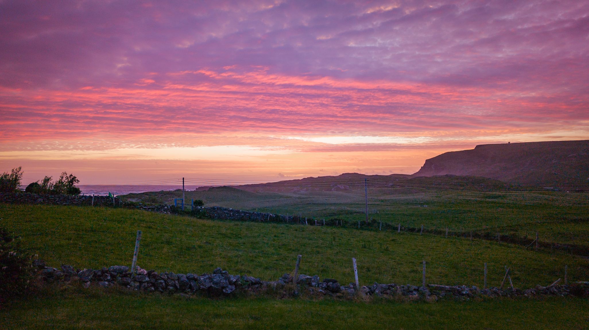 Luí na gréine os cionn na Dumcha, Gleann Cholm Cille, agus dathanna idir bhuí, bhándearg agus dúghorm sa spéir