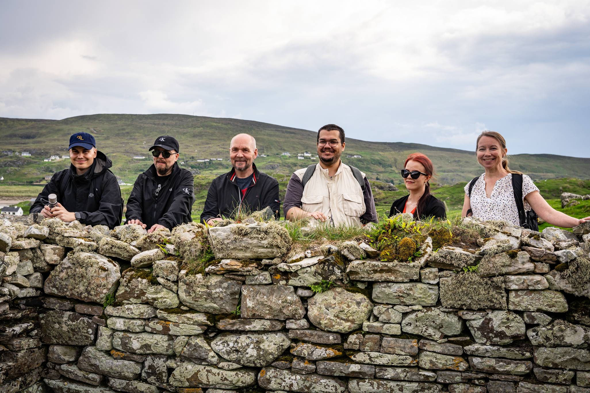 Grúpa as an Fhionlainn ag seasamh ag balla i nGleann Cholm Cille